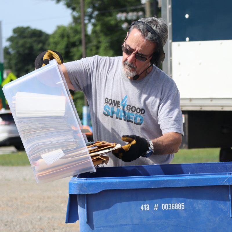 man dumping papers out of clear tote into blue recycling bin